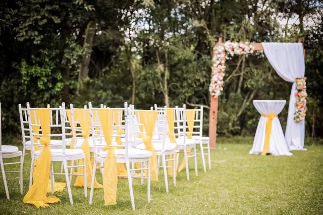 Charming outdoor wedding setup featuring a floral arch and white chairs with yellow sashes.